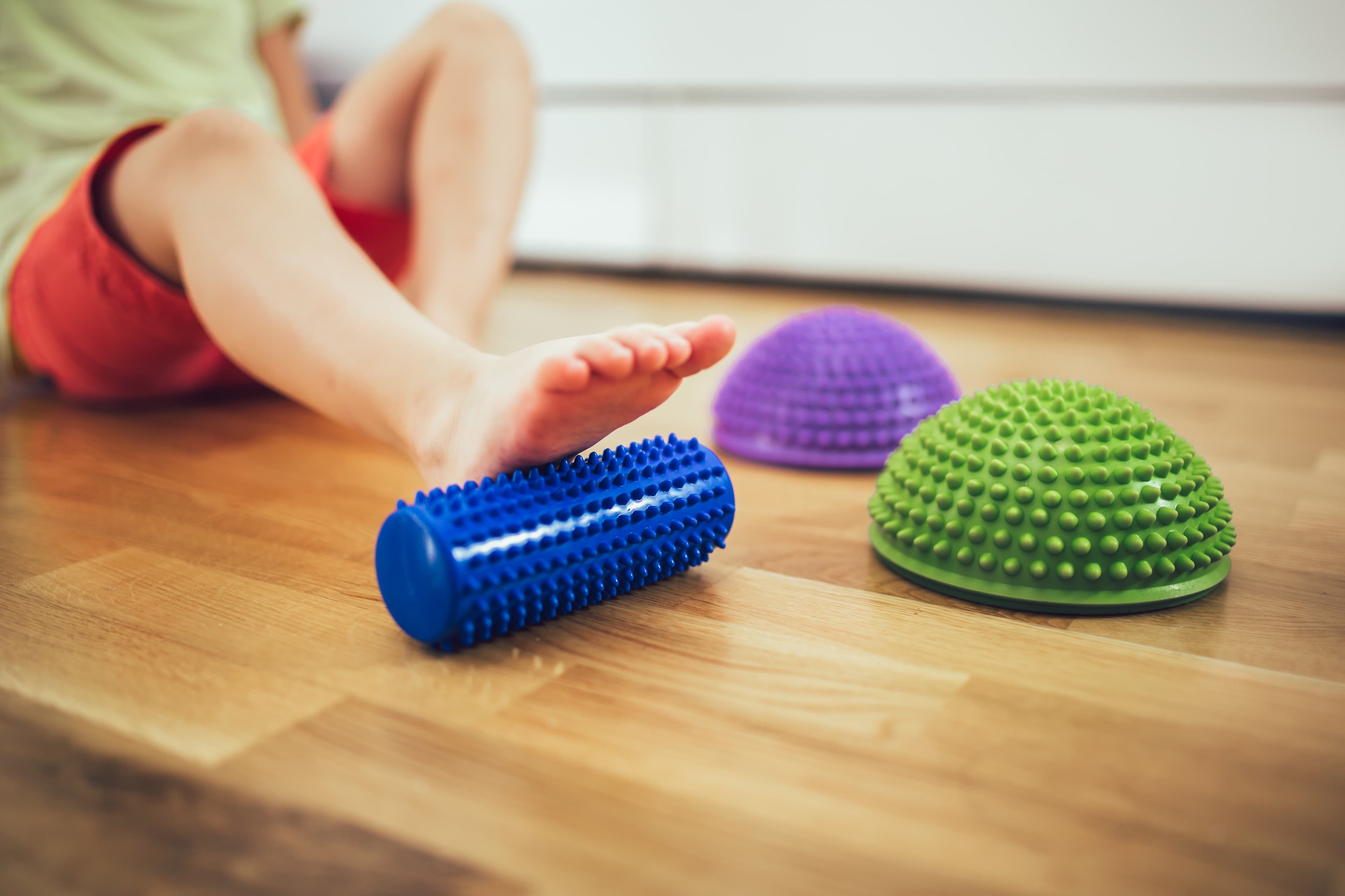 Child's bare foot on a blue spiked roller with green and purple sensory balance pods.