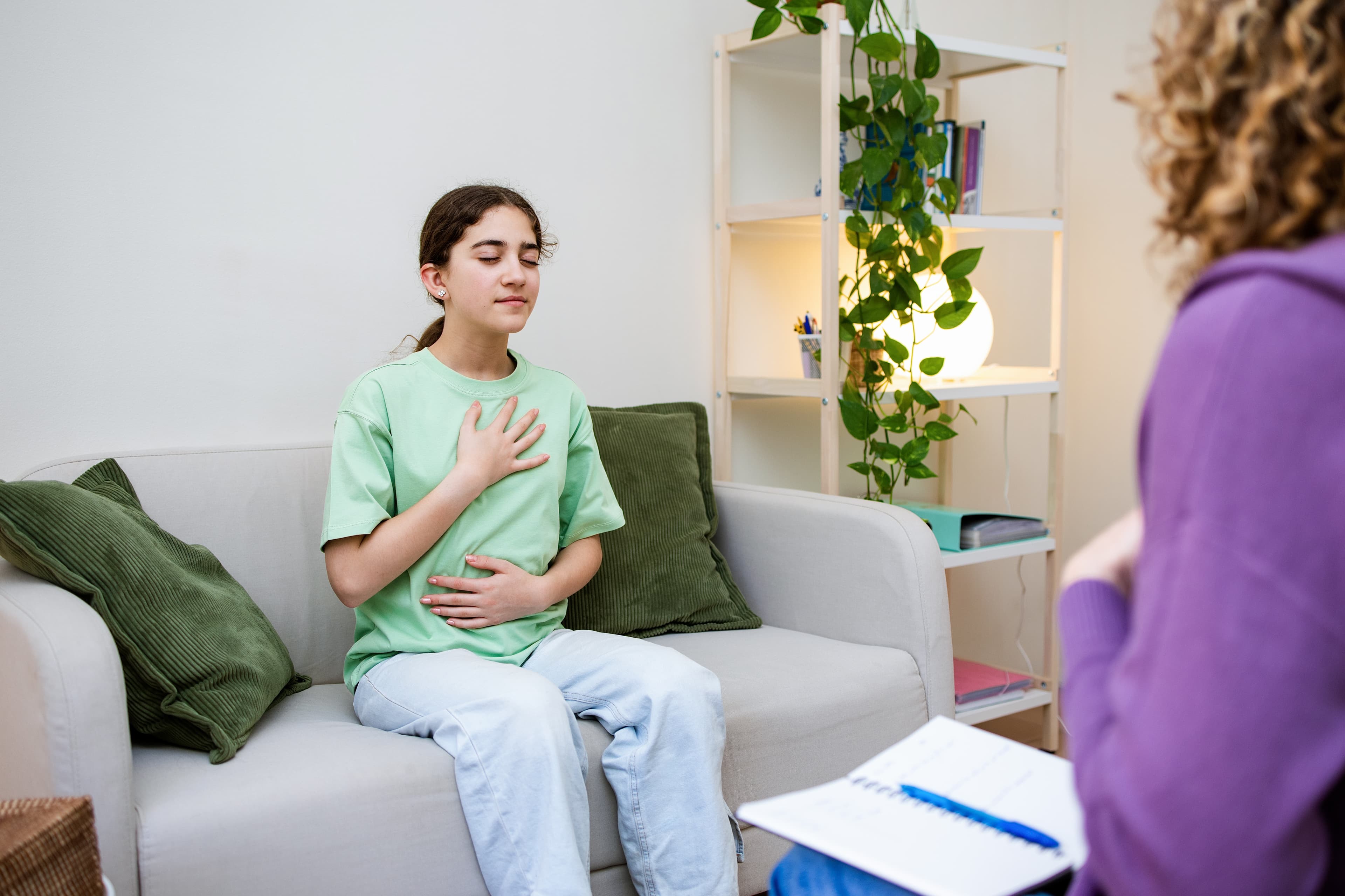 Teenage girl practicing deep breathing with eyes closed during a therapy session with a counselor.